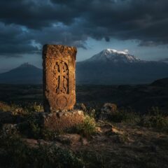 Monumento de pedra Khachkar arménio diante do Monte Ararat representando a história e sobrevivência cultural da Arménia.