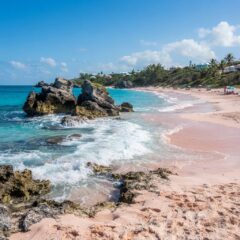 Praia de areia rosa e mar turquesa com formações rochosas nas Bermudas sob luz natural do dia.
